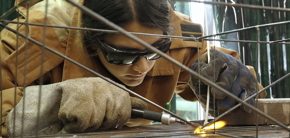close up of a woman using a welding tool while wearing protective glasses and gloves