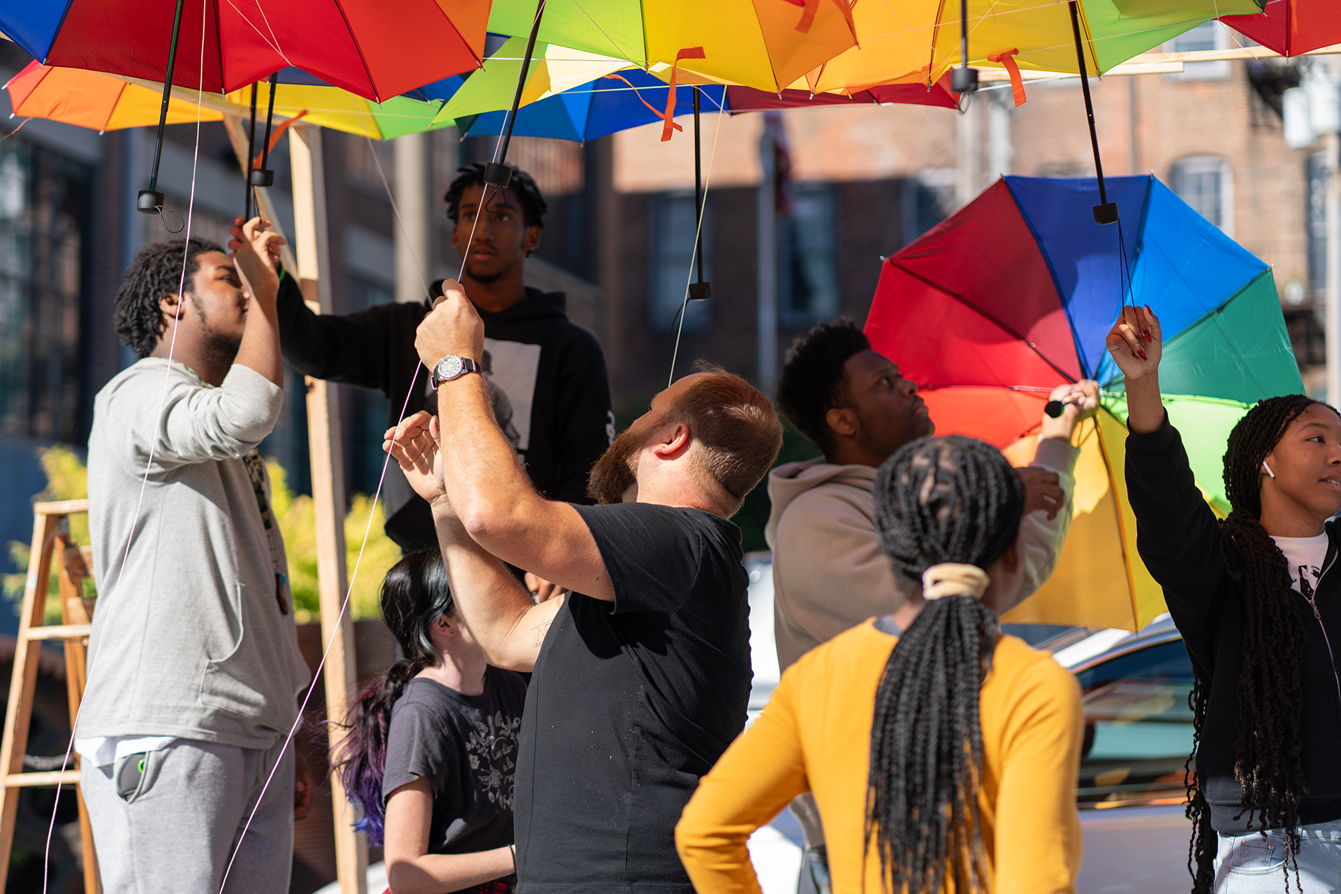 https://aap.cornell.edu/A%20group%20of%20people%20work%20together%20to%20put%20up%20rainbow%20umbrellas