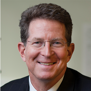 A man with brown hair and glasses wearing a suit and tie.