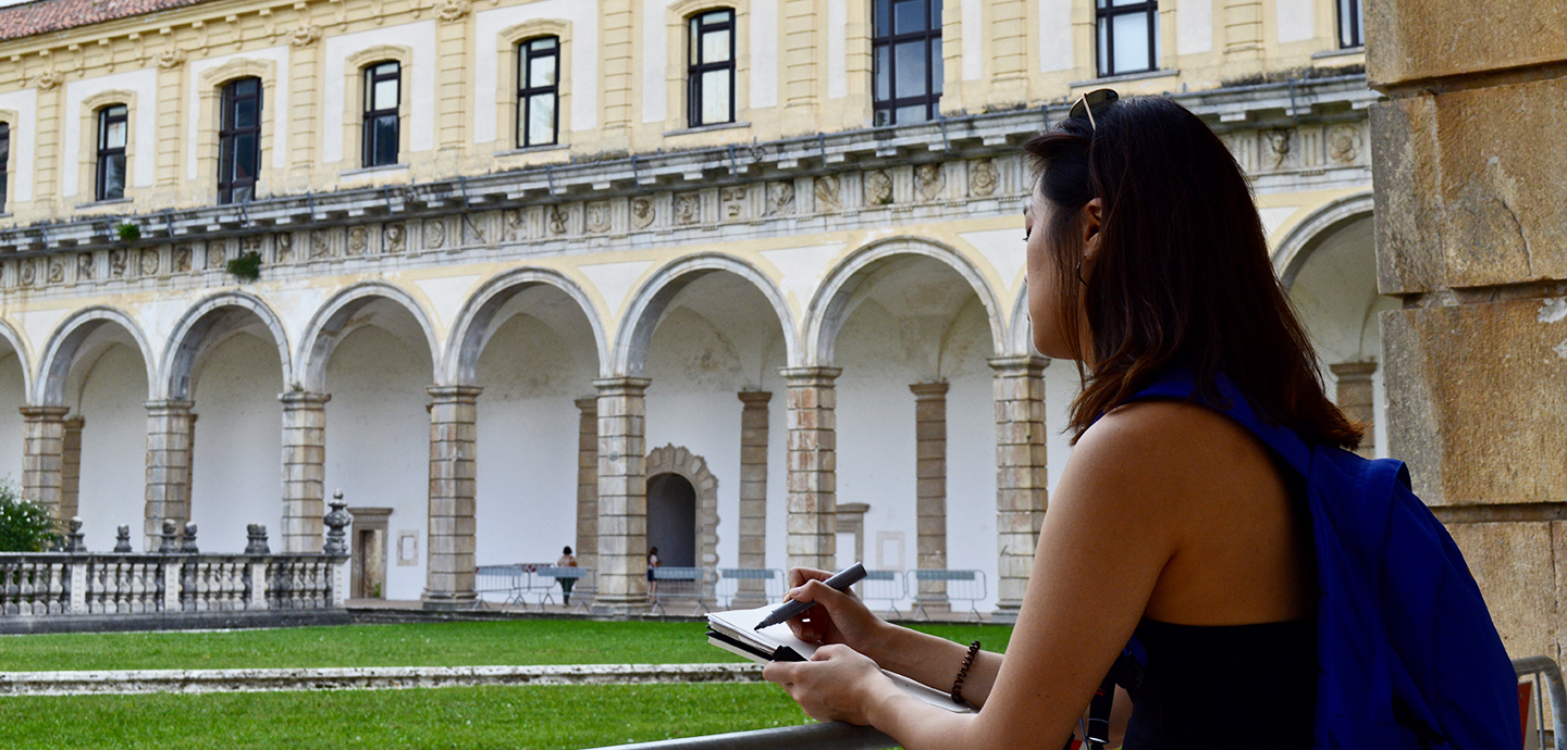 A woman sketching with a Roman collonade in the background