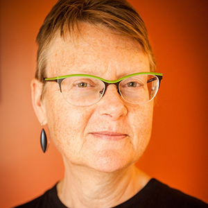 woman with short hair and green glasses against an orange background