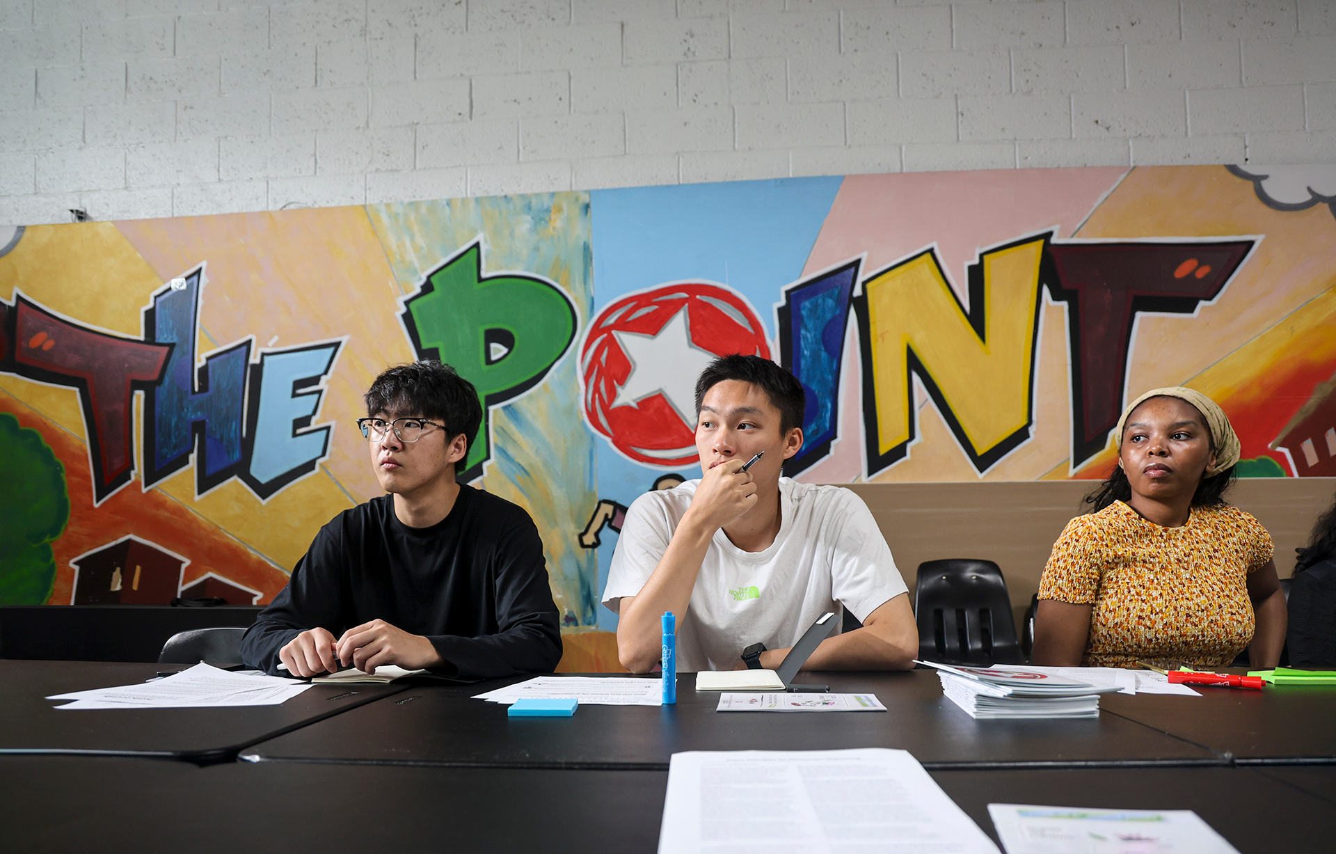 Three students seated at a table with a bright mural behind them.