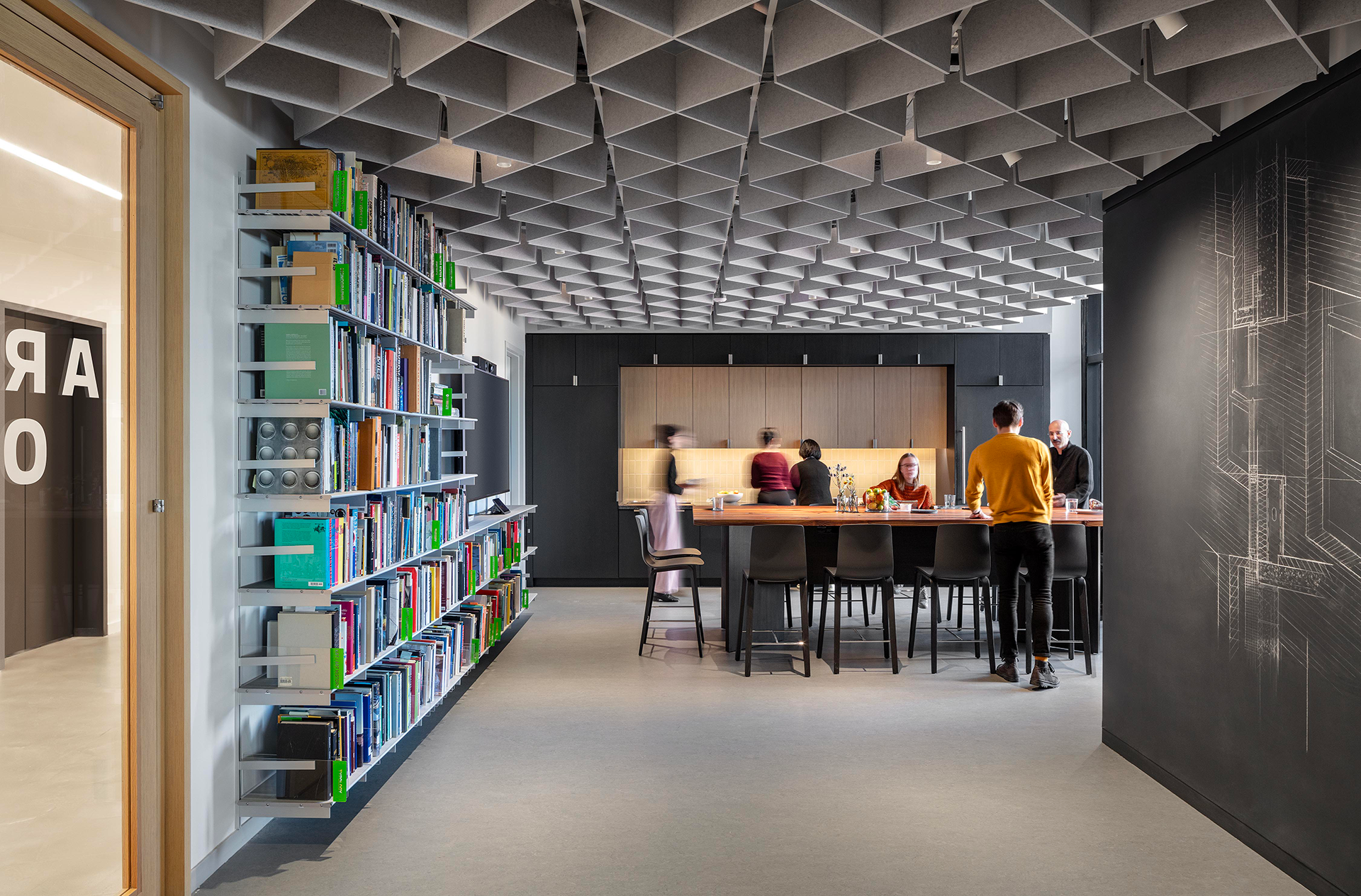 people at work around a table with a bookshelf full of books at left