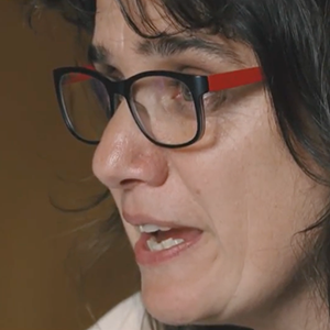 A white woman wearing black and red glasses in profile speaking