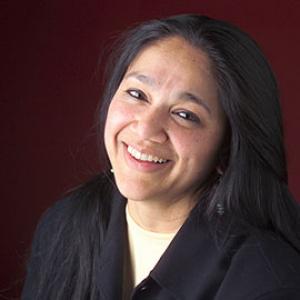 person with long black hair in a black shirt smiling at the camera with head titled to the right