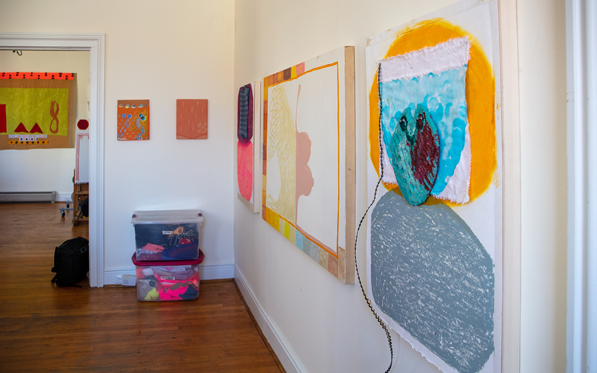 Paintings hung along wall with bins filled with fabric on the floor