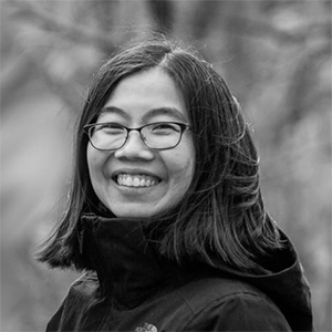 A black and white photo of a woman with shoulder-length dark hair and glasses smiling at the camera.