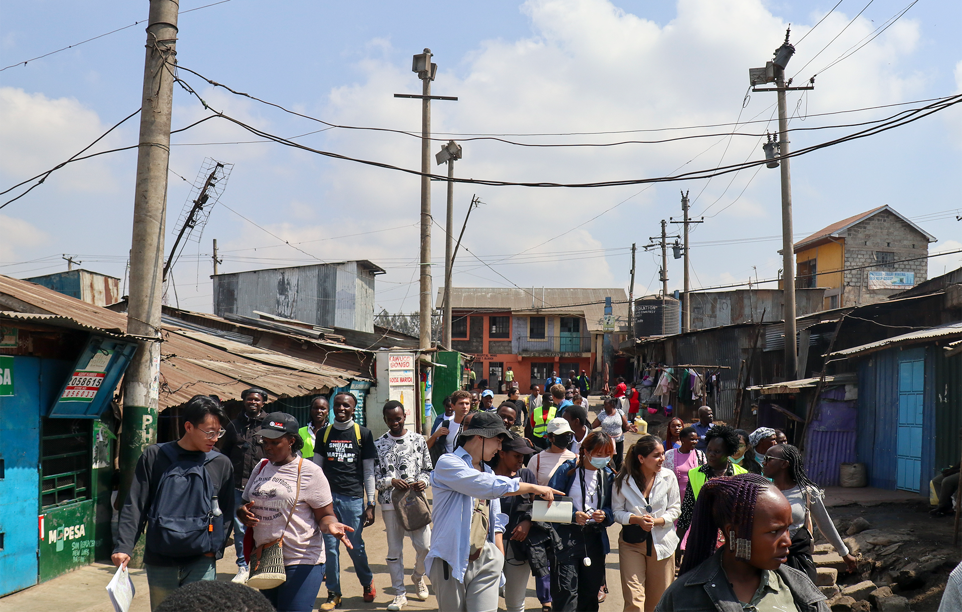 Students walk with local community members down a street between homes and shops