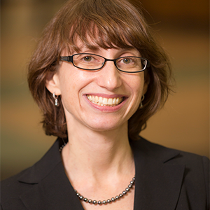 Woman with short brown hair and bangs wearing a dark jacket and glasses