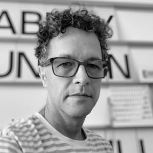 person with short curly hair and glasses wearing a horizontal striped shirt looking at the camera