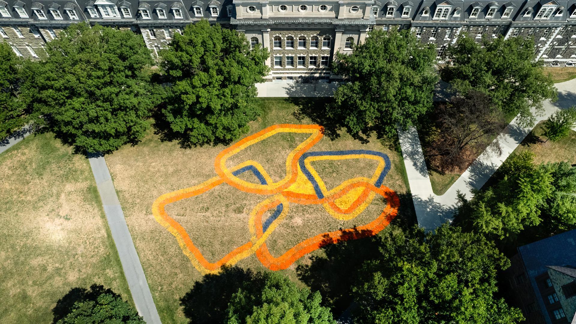 Aerial view of a geometric painting made on the lawn in front of a large brick building.