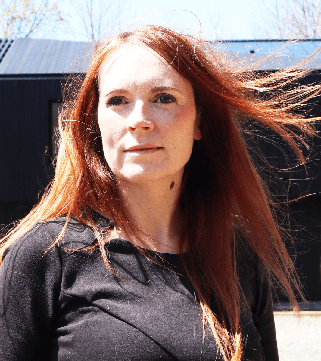 A person with long red hair a black shirt standing in front of a building.