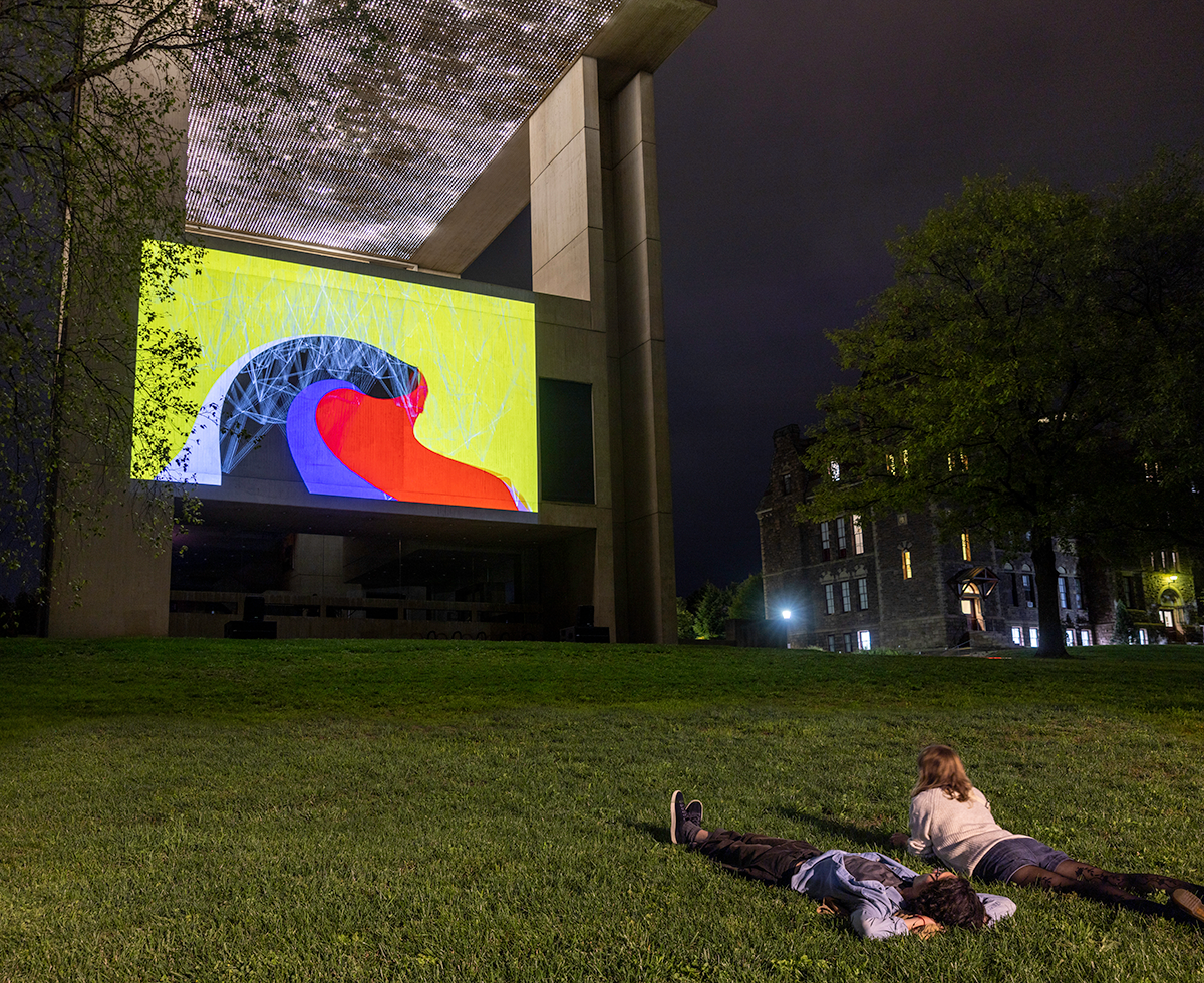 People lying in the grass at night watching a projected image on the side of a building