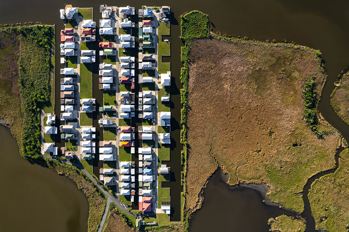 Aerial view of sunny house roofs surrounded by water and grassland.