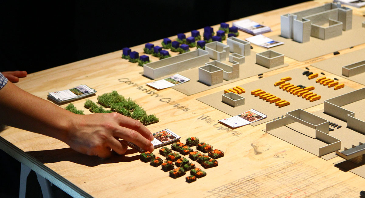hand moving pieces on an urban scale model on a wood table