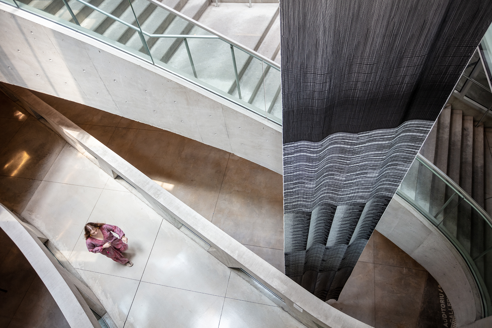 Aerial view of hanging black and white tapestry with woman passing by.