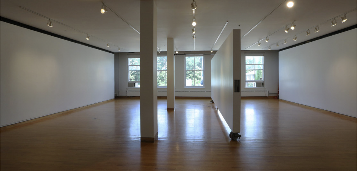 Room with white walls and wood floor, two columns, and a moveable wall are in the center and there are three windows on the far wall