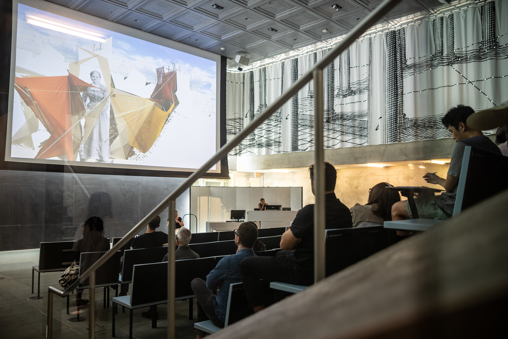 Attendees gathered in a lecture hall listening to a talk while viewing a large projection on a screen