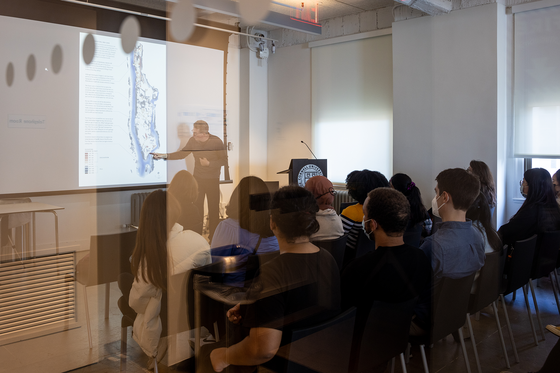 Man standing in front of a screen lecturing to a group of students