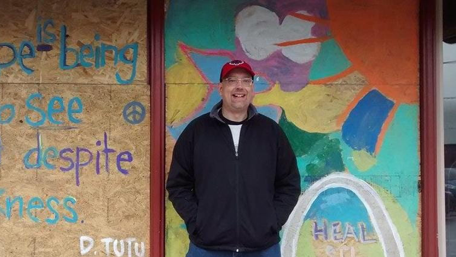 A man wearing a red hat smiling in front of a mural.