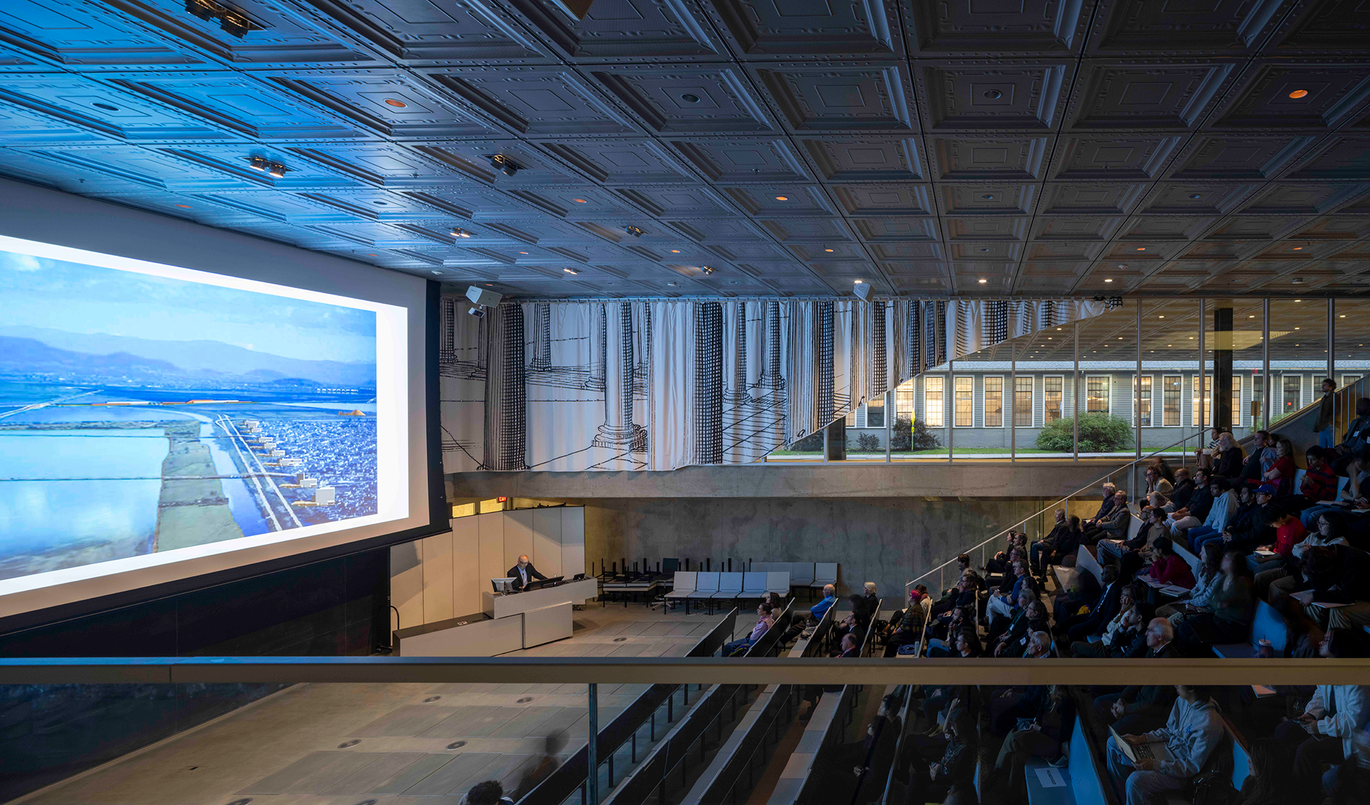 audience gathered in a lecture hall viewing a speaker and large screen projection