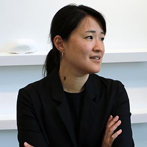 portrait of a woman with black hair wearing a black shirt and jacket with her arms crossed in front of her