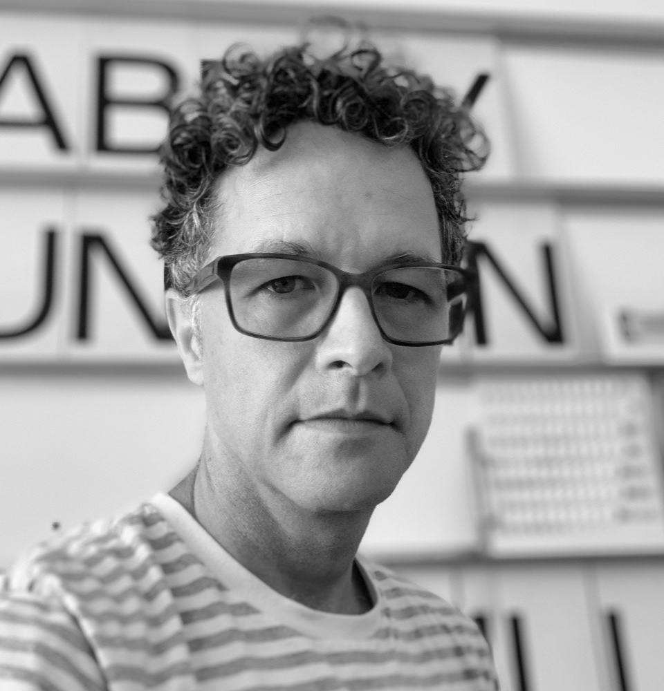 A man with curly hair wearing glasses and a striped shirt.