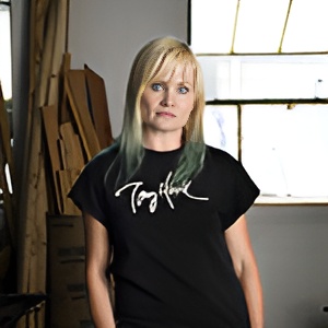 A person with long blonde hair wearing a black t-shirt with white text.
