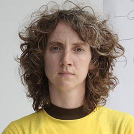 A person with curly hair wearing a yellow shirt with a black stripe around the neck.