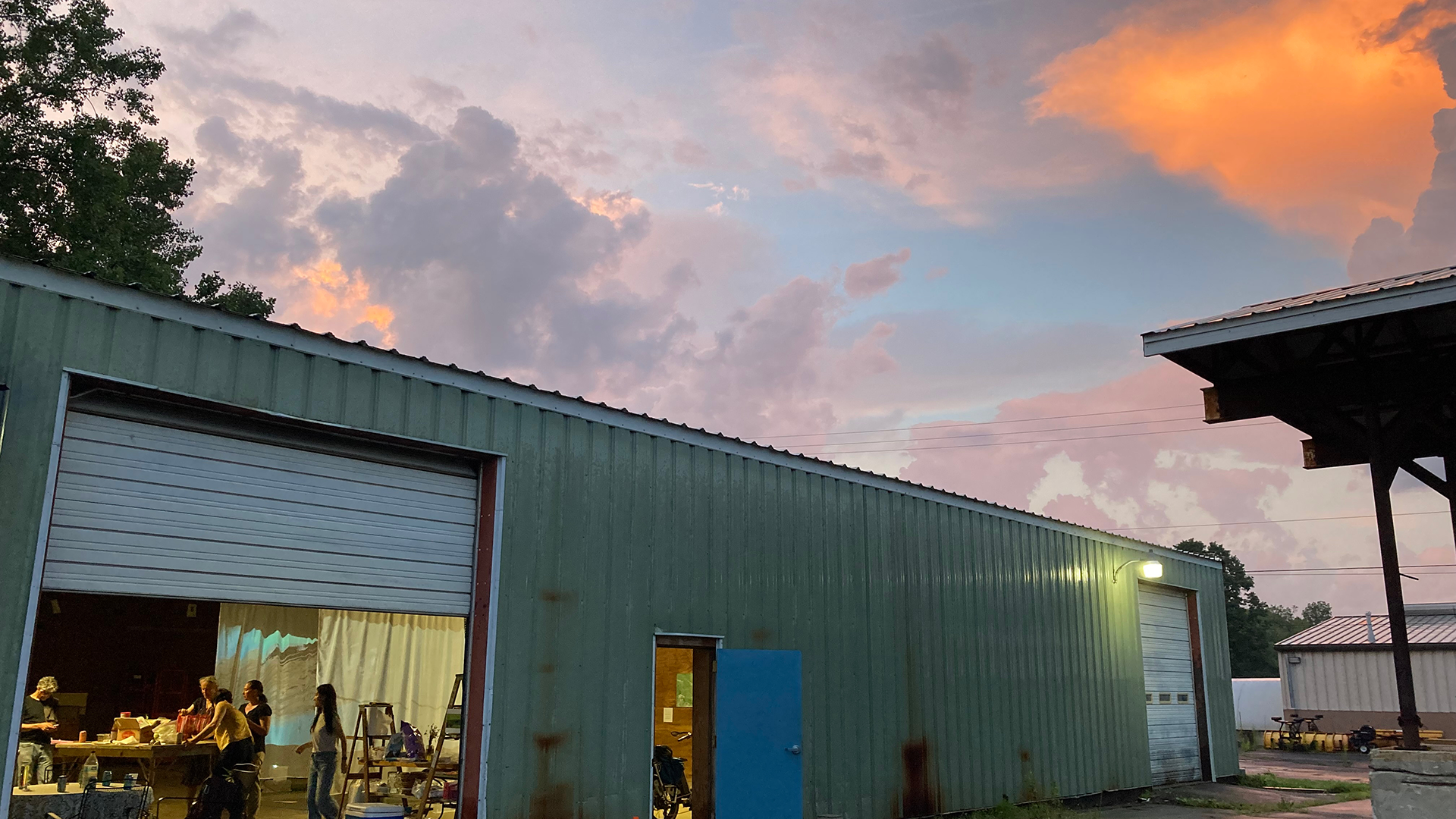 Metal-sided garage space with door rolled up and people inside working at a table