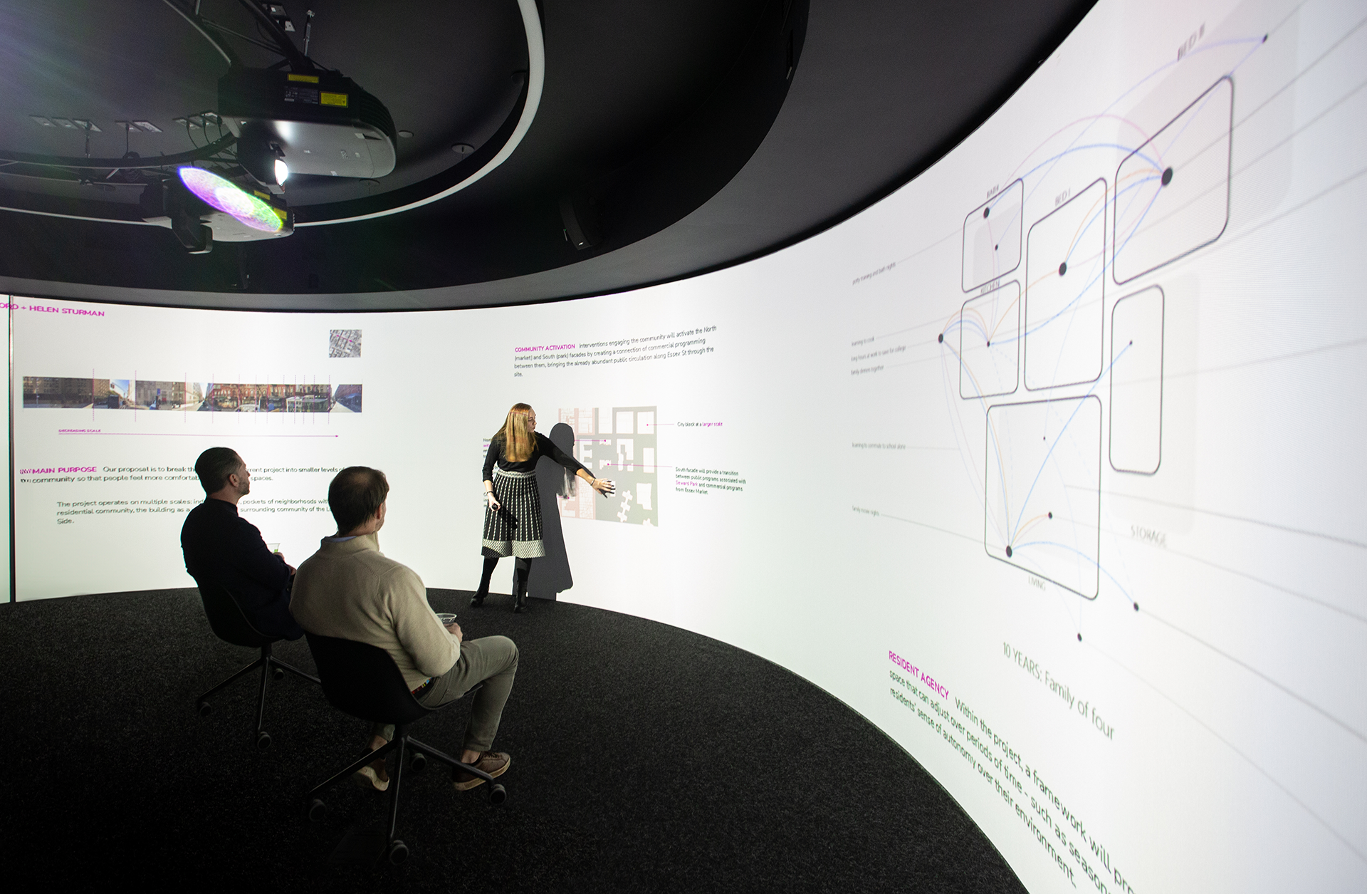Student giving a presentation to two people in front of a large digital projection.