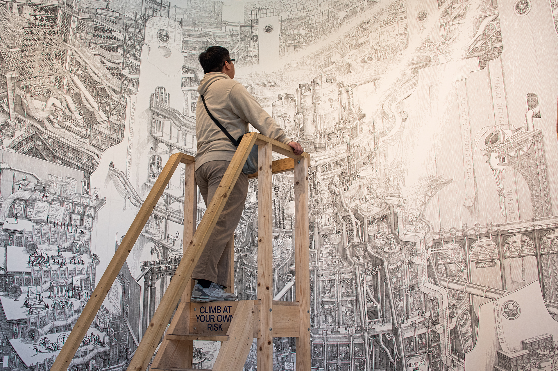 Person on a wooden ladder examining a black and white artwork.