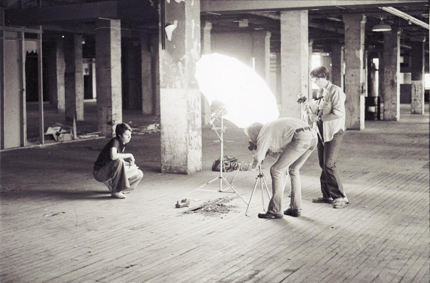 Three people looking at a pile of dirt with a large umbrella light while taking photos.