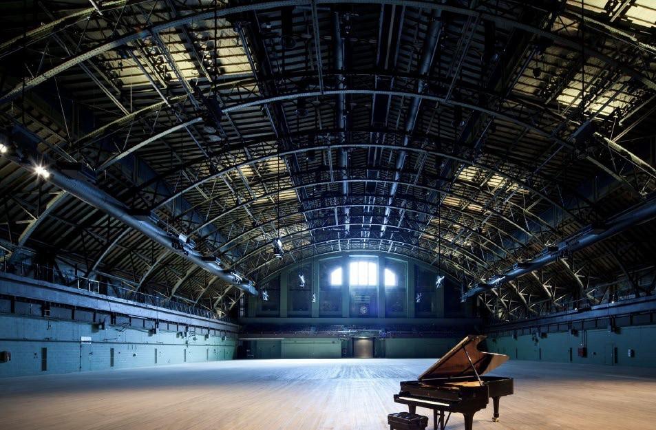 a grand piano with the top opened on an empty stage in an empty curved-roof atrium