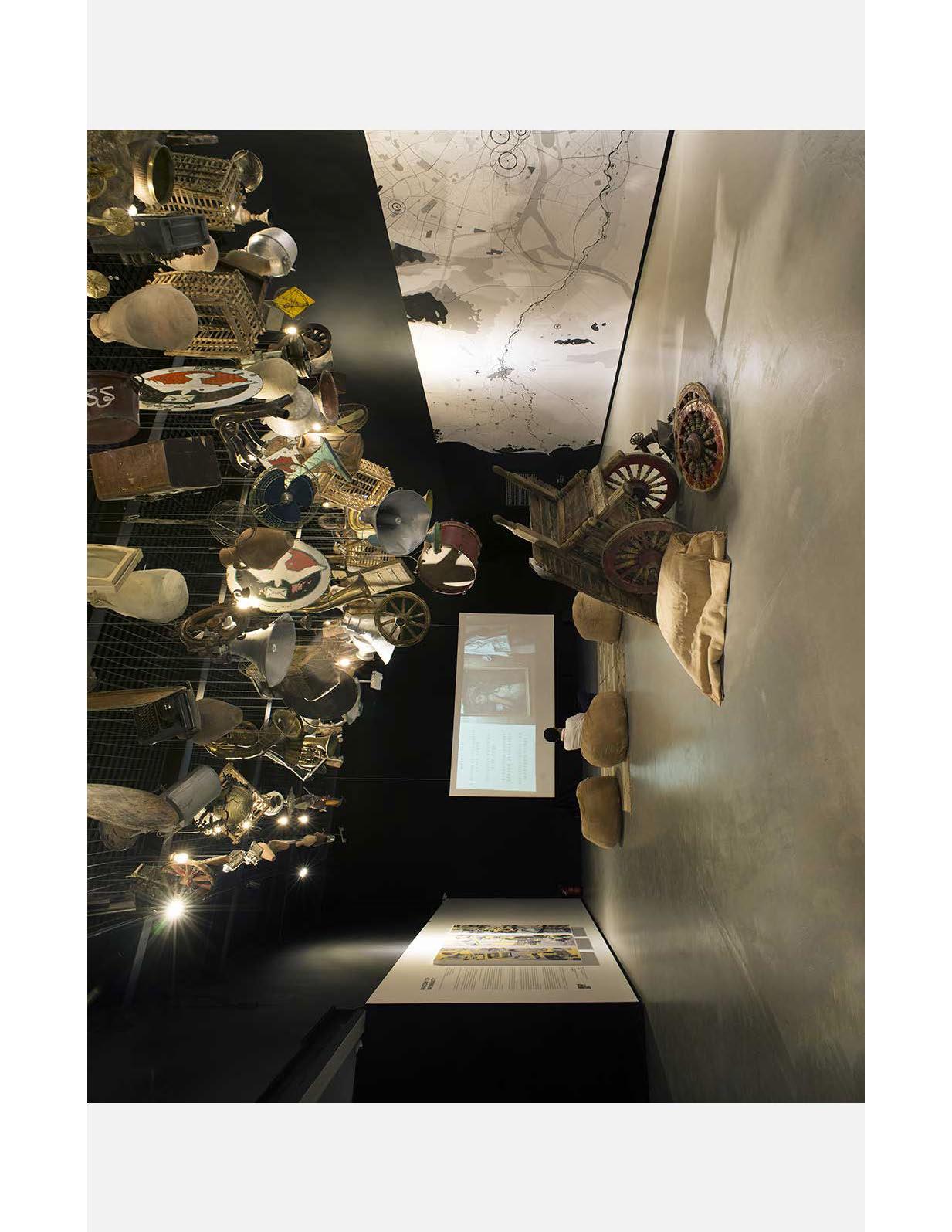Objects in a gallery space with a screen and items hanging from the ceiling.