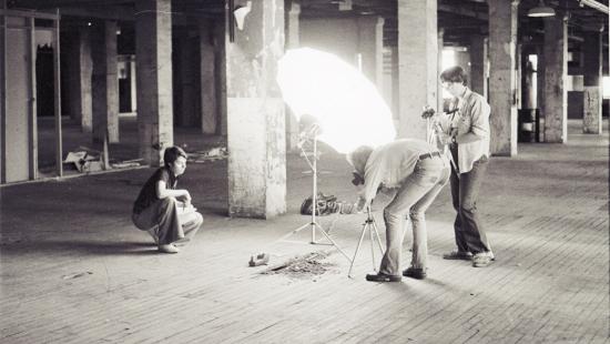 Three people looking at a pile of dirt with a large umbrella light while taking photos.