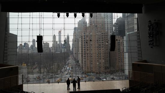 Three people on a stage in a glassed-in room overlooking a city