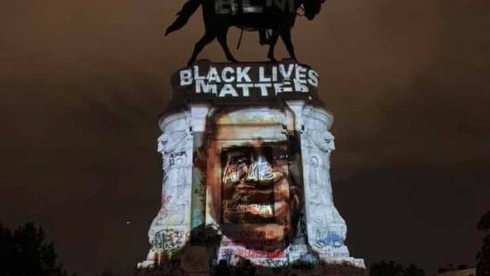 A person on horseback on a massive plinth and the face of a person projected on the plinth.
