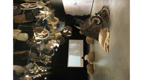 Objects in a gallery space with a screen and items hanging from the ceiling.