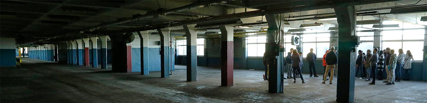People standing within a concrete structure with pillars and large windows.