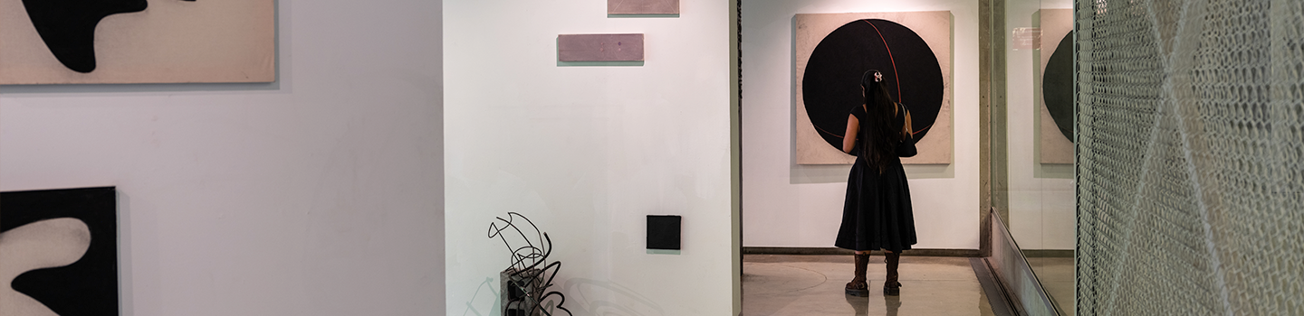 A woman dressed in black looks at a painting hung in a gallery.