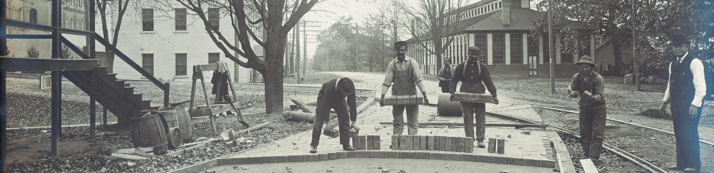 Black and white photo of men laying first bricks for building construction