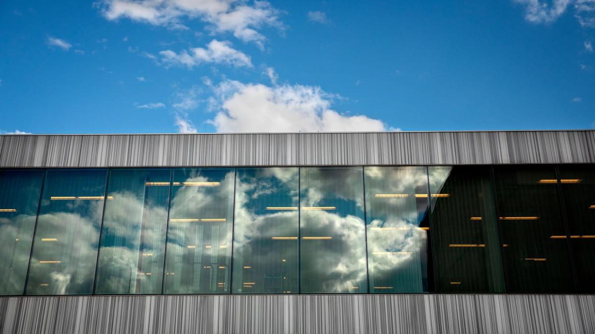 A bright blue sky with white clouds behind the siding of a glass and metal building.