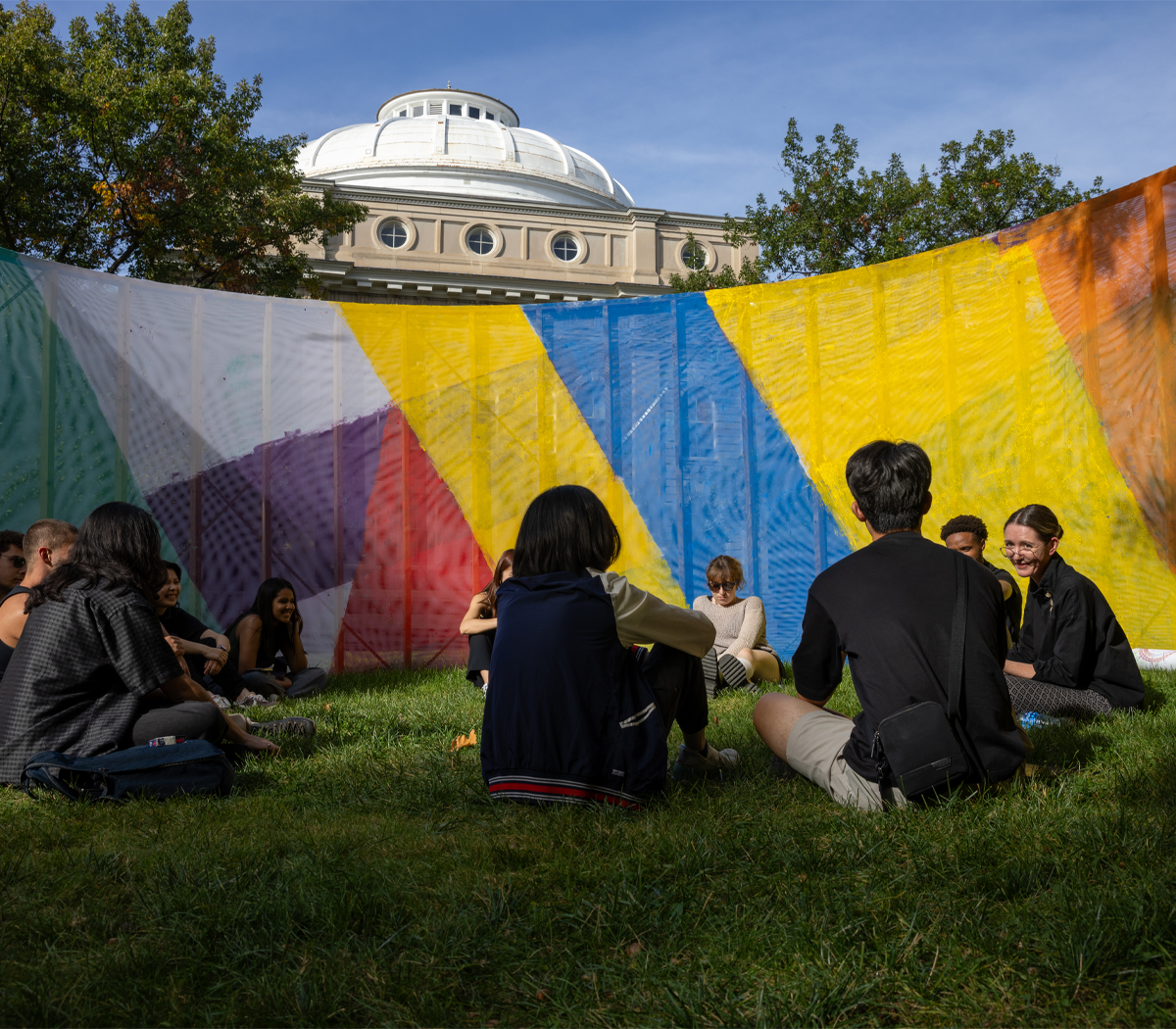 People sitting on the grass surrounded by a large colorful wall.