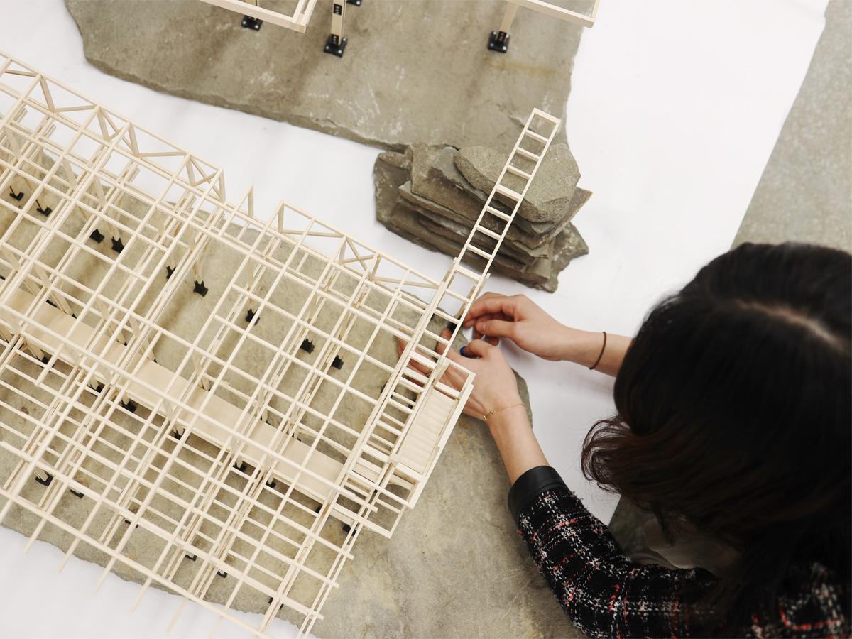 A person working on a wooden and stone architectural model.