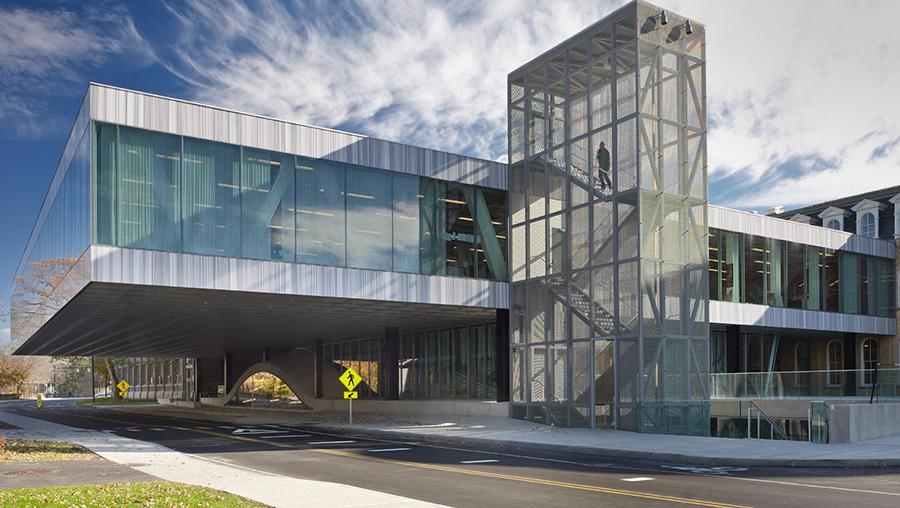 A modern glass building cantilevered over a road with a metal stair tower attached