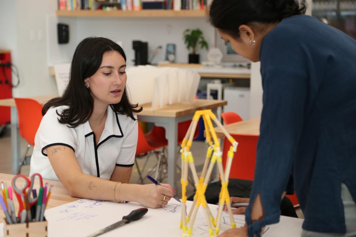 Two people collaborate in a design studio, sketching ideas beside a small structural model.