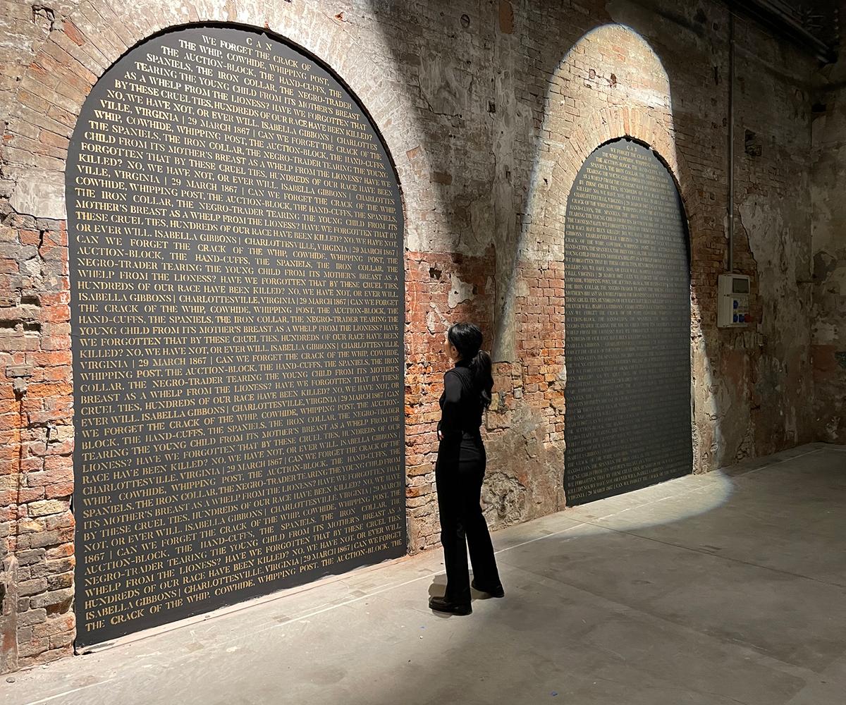 Person looking at a wall of names written on a black backdrop within a brick archway