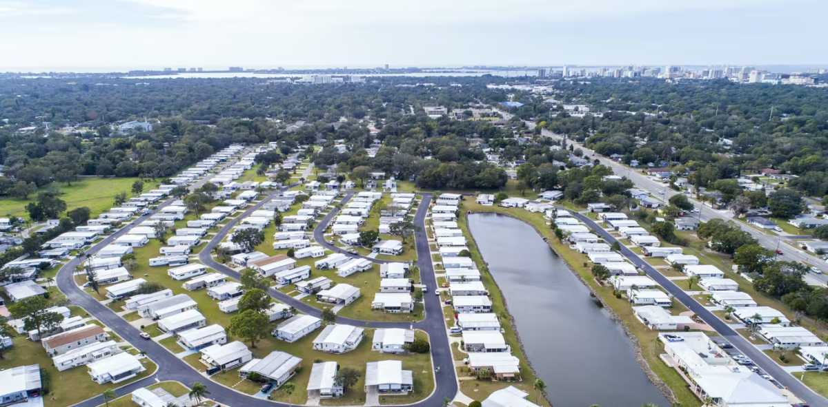 A series of white manufactured homes surrounded by trees with a pond in the center.