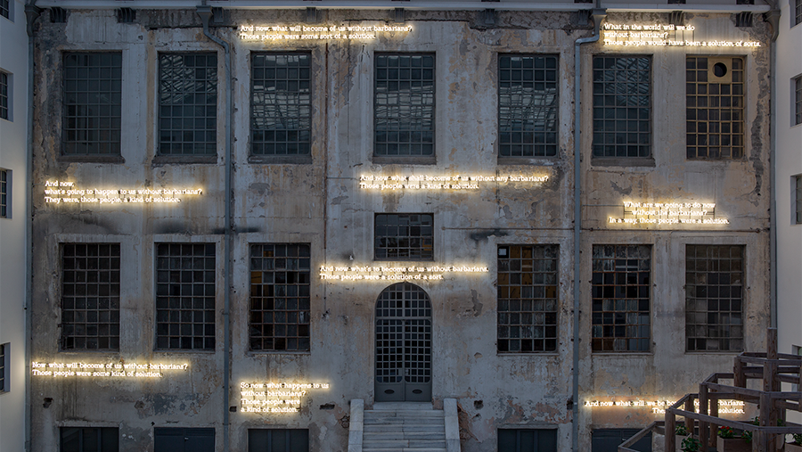 Text written in neon lettering affixed to a cement building façade